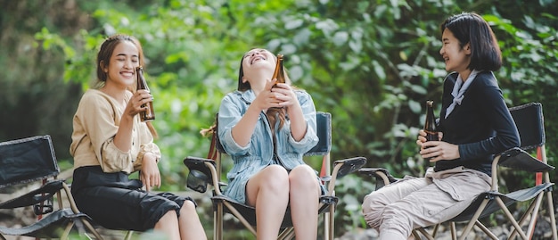 group of young asian women drink beer in their chairs and soaked their feet in the stream while camping in the nature park they are enjoy to talking and laugh fun together
