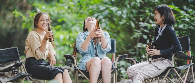 若いアジア人女性のグループは、自然公園でキャンプしている間、椅子でビールを飲み、小川に足を浸しました。彼らは一緒に話したり笑ったりするのを楽しんでいます。