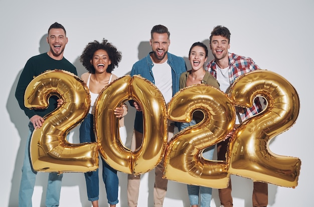 Group of young beautiful people in casual clothing carrying gold colored numbers and smiling