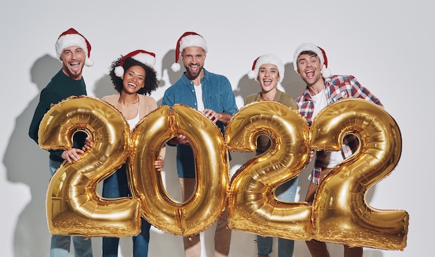 Group of young beautiful people in christmas hats carrying gold colored numbers and smiling