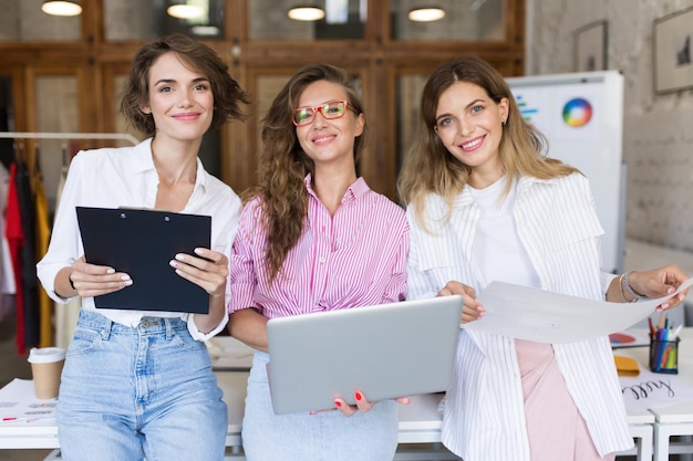 Group of young beautiful stylish women with laptop and folder ha