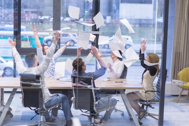 Group of young business people throwing documents and looking happy while celebrating success at their working places in startup office