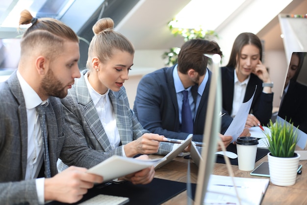 Group of young business people working, communicating while sitting at the office desk together with colleagues.