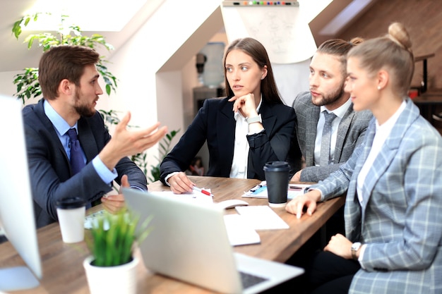 Gruppo di giovani uomini d'affari che lavorano, comunicano seduti alla scrivania dell'ufficio insieme ai colleghi.