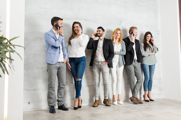 Group of young businesspeople standing against the wall and using their mobile phones