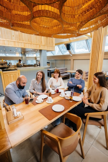 A group of young cheerful friends is sitting in a cafe talking and eating pizza