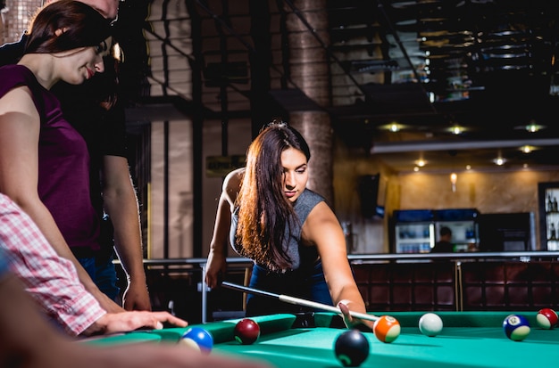 Group of young cheerful friends playing billiards.