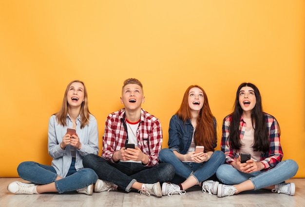 Group of young cheerful school friends using mobile phones