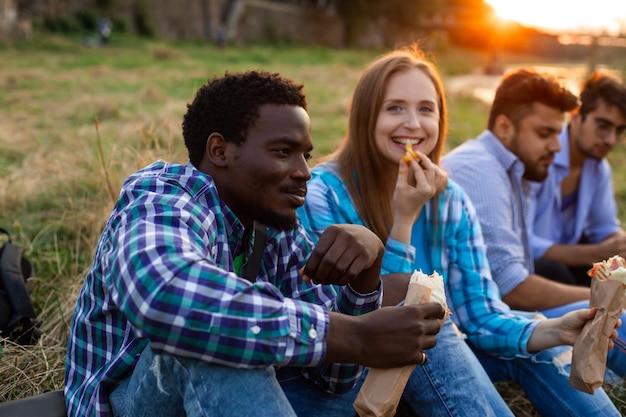 The group of young diverse people eating fastfood on nature