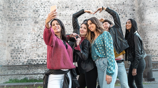 Group of young friends in the ancient city center taking a\
selfie with the smart phone - seven people have fun together