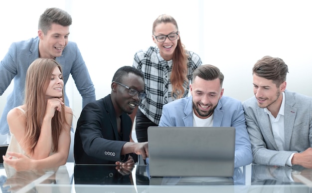 A group of young friends four men and two women looking at a laptop sitting together at a table in a office