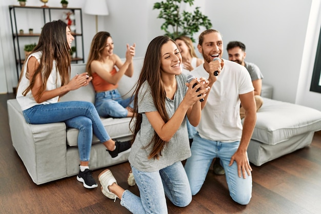 Group of young friends having party singing song using microphone at home