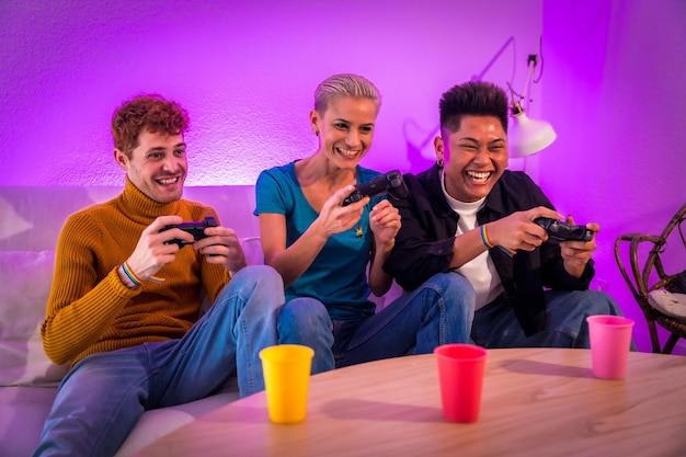 Photo group of young friends play video games together on the sofa at home purple led