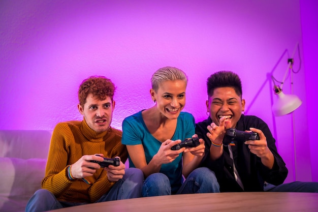 Group of young friends playing video games together on the sofa at home purple led having fun pushing