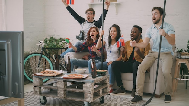 Group of young friends sports fans with norwegian national\
flags watching sport championship on tv together and happy about\
winning favourite team at home