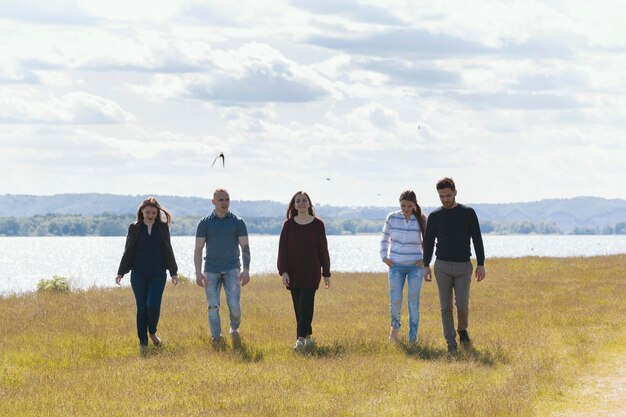 Photo group of young friends walking on the hill on the background wide river