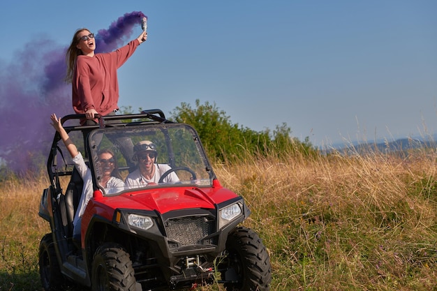 group of young happy excited people having fun enjoying beautiful sunny day holding colorful torches while driving a off road buggy car on mountain nature