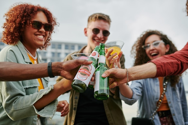 Gruppo di giovani felici multiculturali che tintinnano con birra e cocktail