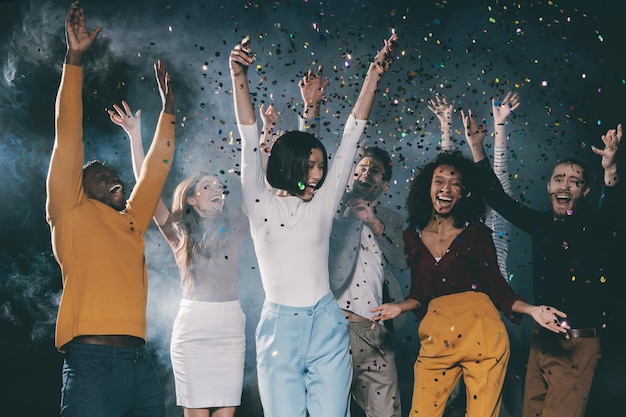 Group of young happy people dancing and throwing confetti while having fun in night club together