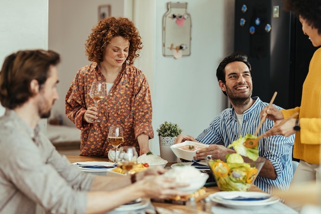 ダイニングテーブルでランチタイムに楽しんでいる若い幸せな人々のグループ。