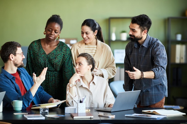 Group of young intercultural creative designers gathered by workplace consulting or sharing ideas at