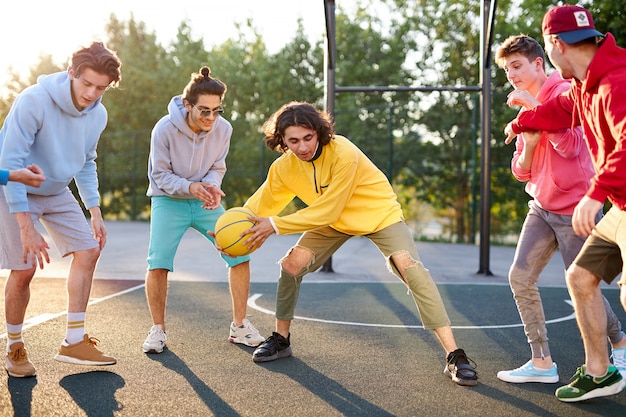 Group of young male teenagers in colourful hoodies playing basketball outdoors in the street