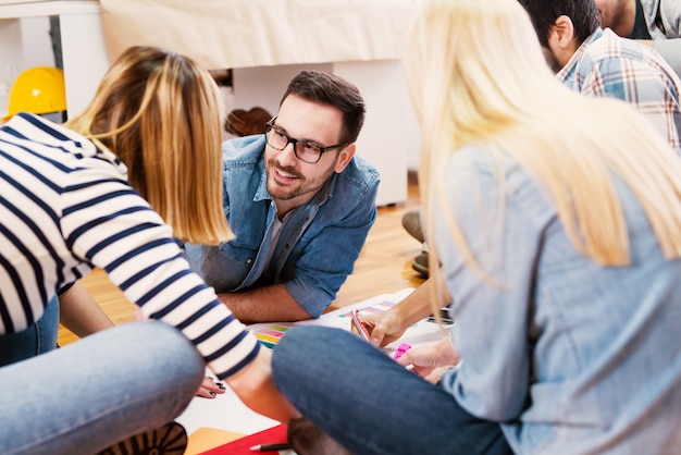 Group of young modern designers sitting on a floor and making new plans.