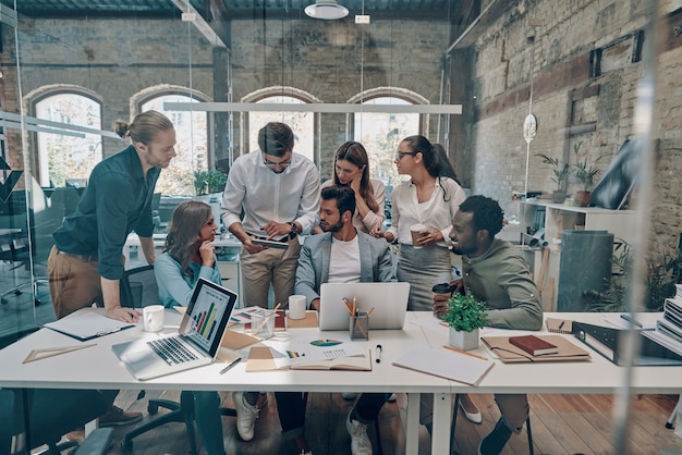 Group of young modern people in smart casual wear communicating and using modern technologies while working in the office