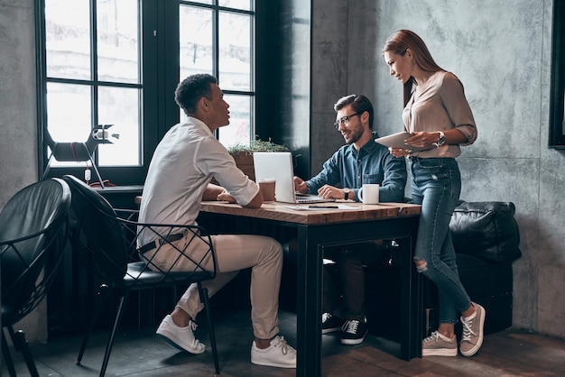 Group of young modern people in smart casual wear discussing something while working in office