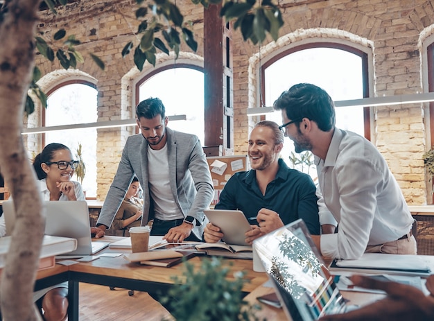 Group of young modern people in smart casual wear talking business ideas and smiling while working in the office