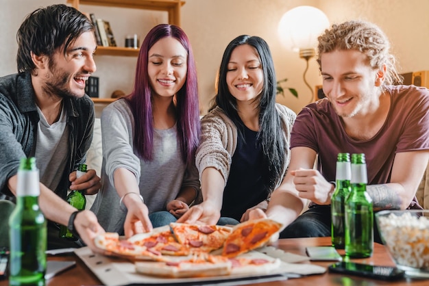group of young multi ethnic friends with pizza and beer celebrating at home