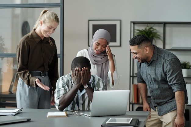 Group of young multicultural students laughing at black man hiding his face