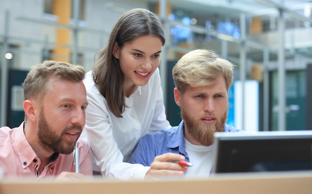 Group of young people in casual wear sitting at the office desk and discussing something while looking at PC together.