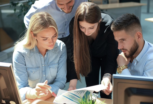 Group of young people in casual wear sitting at the office desk and discussing something while looking at PC together