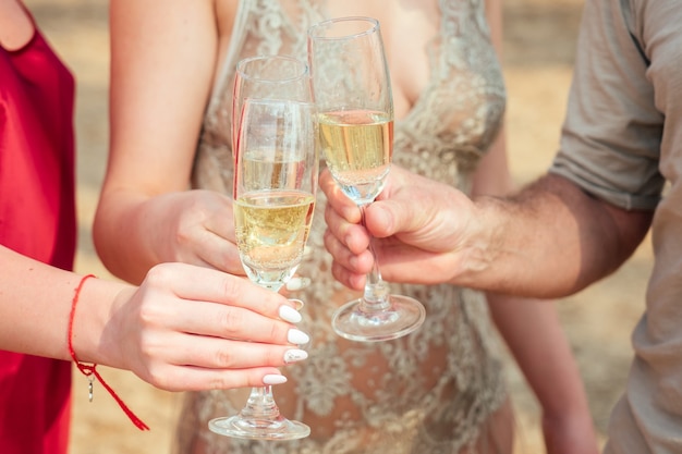 Un gruppo di giovani festeggia con bicchieri di champagne sulla spiaggia. bicchieri di vetro con spumante nelle mani di donne e uomini in vacanza.