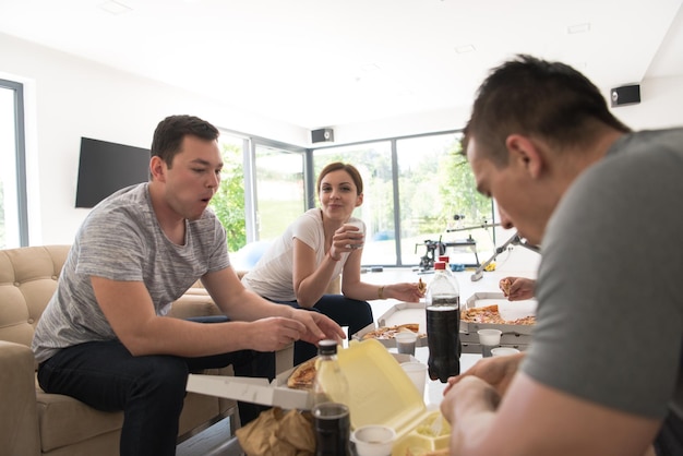 a group of young people cheerfully spending time while eating pizza in their luxury home villa