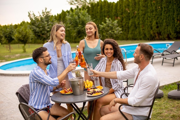 Group of young people cheering with cider by the pool in the garden