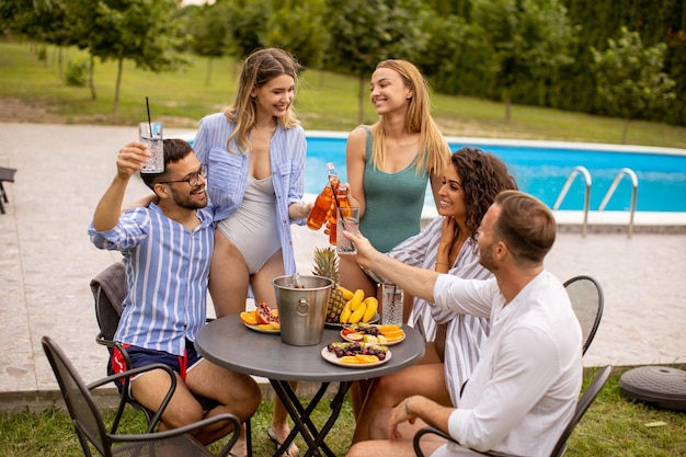 Group of young people cheering with cider by the pool in the garden