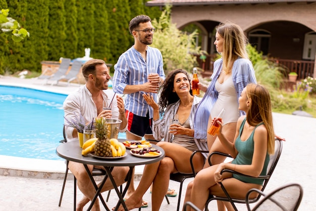 Group of young people cheering with cider by the pool in the garden