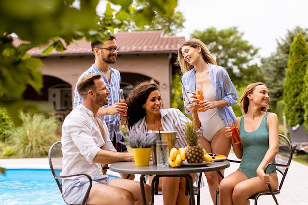 Group of young people cheering with cider by the pool in the garden