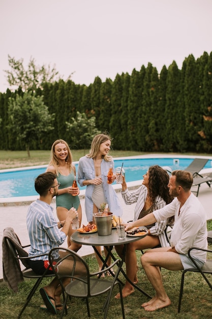 Group of young people cheering with cider by the pool in the garden