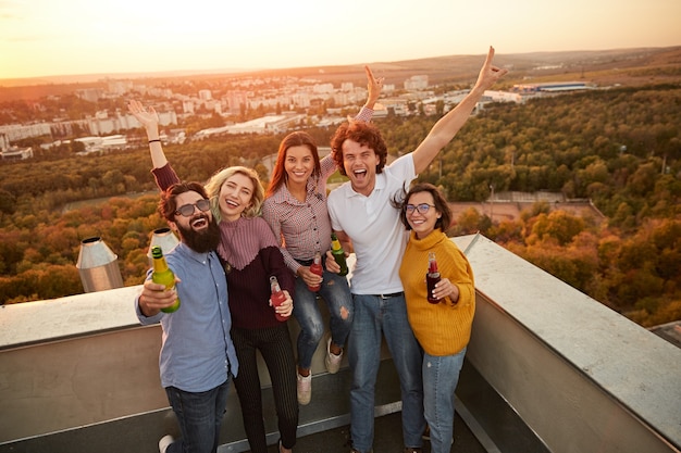 Группа молодых людей, пьющих пиво и отдыхающих вместе на крыше