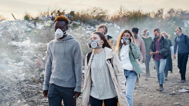 쓰레기 처리장에서 유독한 연기를 통과하는 방독면에 있는 젊은이의 그룹