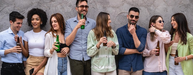 Group of young people having fun standing against a wall\
drinking beers, talking and having fun together - youth friendship\
concept