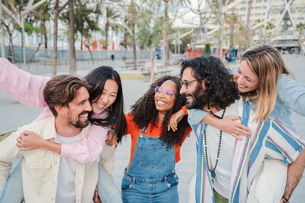 Group of young people having fun together happy men giving their girlfriends a piggyback ride