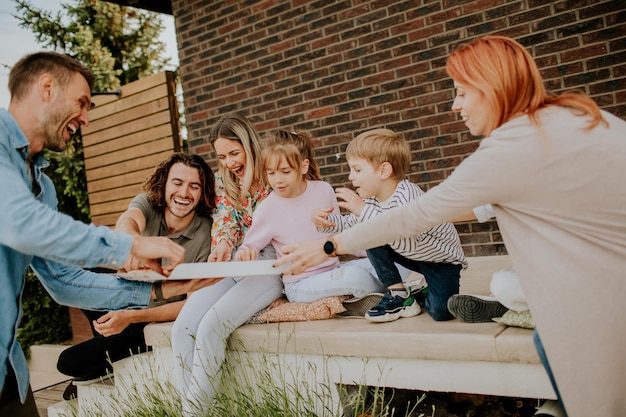 Group of young people and kids eating pizza in the house backyard