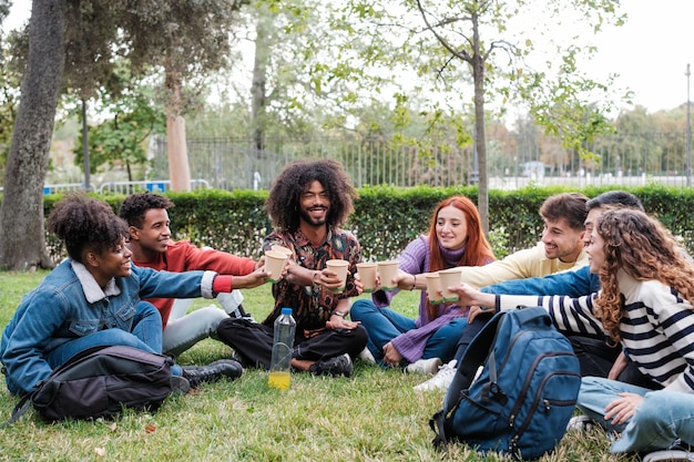 Photo group of young people meeting outdoors in the park toasting with recyclable glasses lifestyle