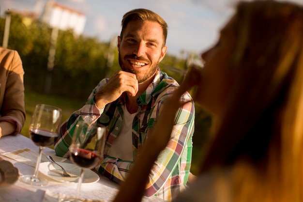 Group of young people sitting by the table and drinking red wine in the vineyard