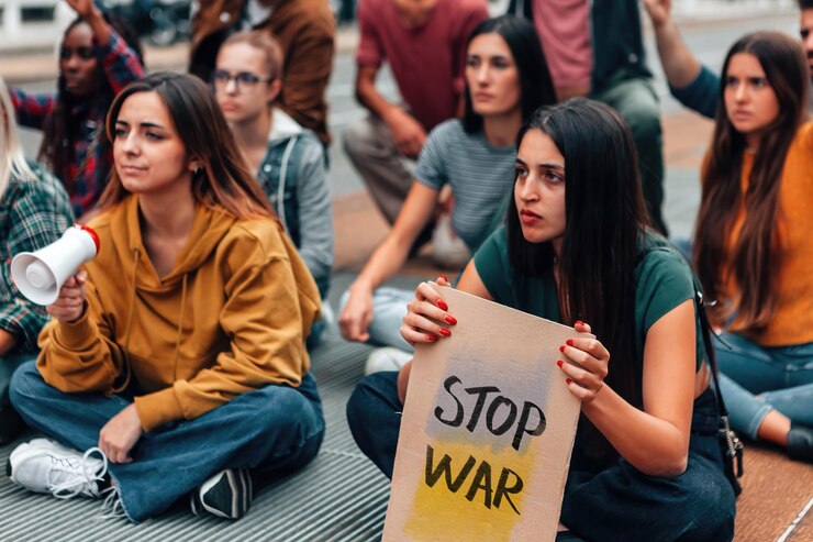 Group of young people sitting on the street protesting for peace in Ukraine cardboard with no war text and Ukrainian flag colors
