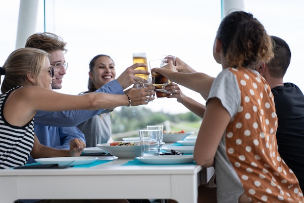 Group of young people sitting at a white table with empty plates toasting